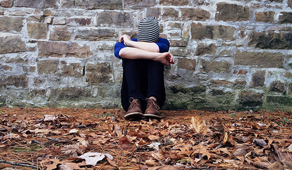 一个悲伤的年轻人靠在石墙上坐着。