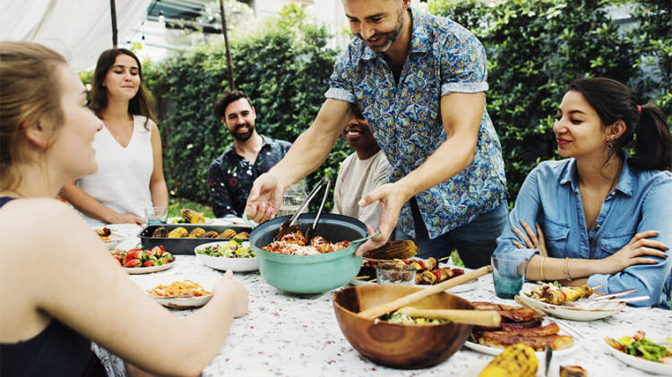 在野餐桌上摆着食物的夏日烧烤会上，一群微笑的朋友。