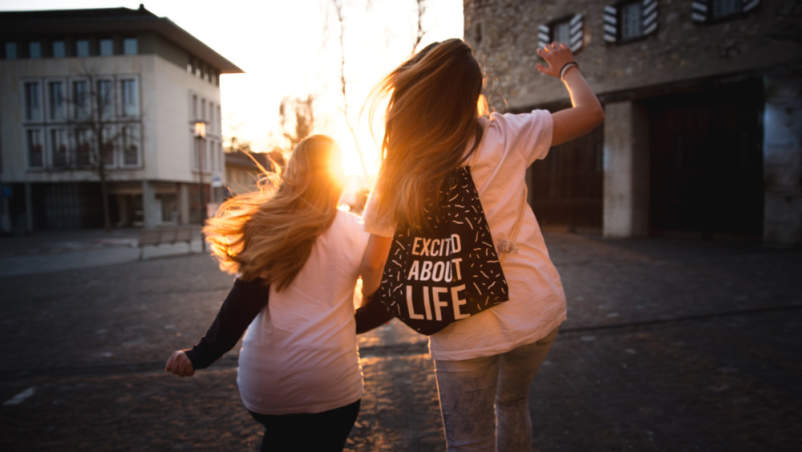 两个年轻的女人一起跳，一个背着背包，上面写着对生活的兴奋
