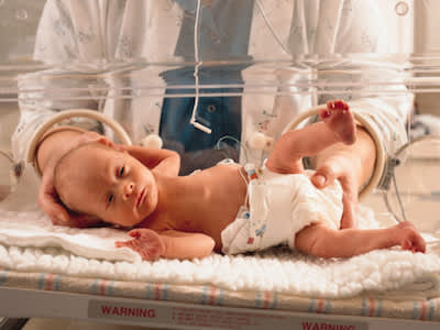 早产婴儿躺在医院的保温箱里，医生站在后面伸出援助之手。