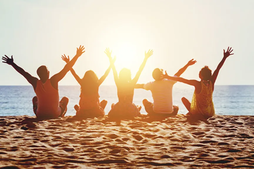 愉快的小组坐海滩举的胳膊的青年人在阳光下。