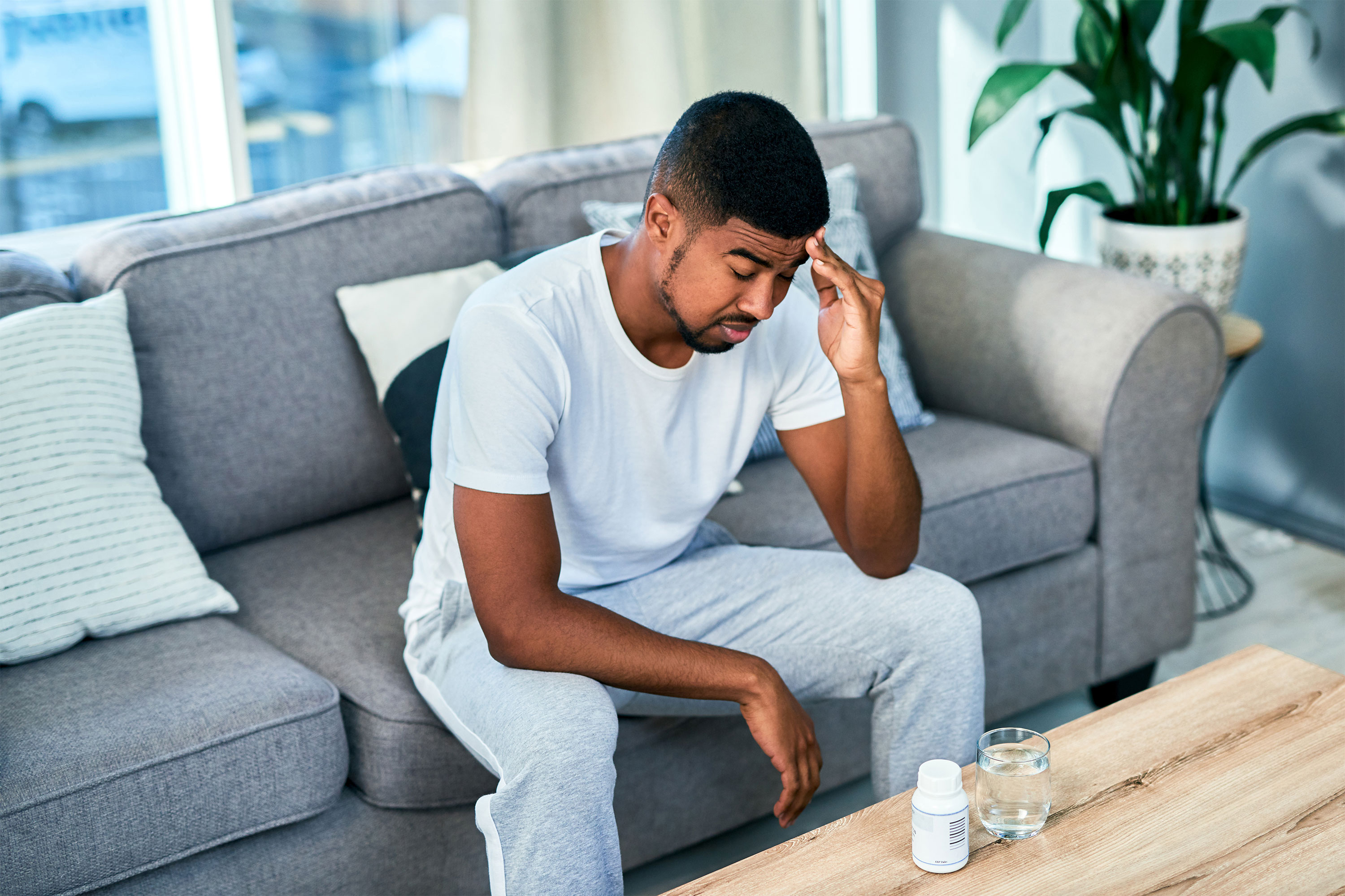 一个男人坐在沙发上，面前放着药和一杯水