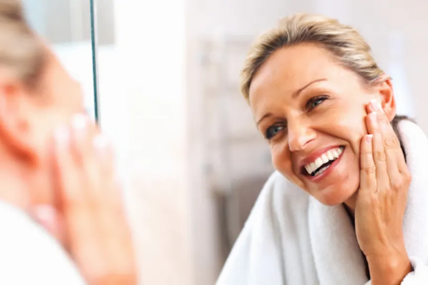 Happy older woman examining skin in mirror.