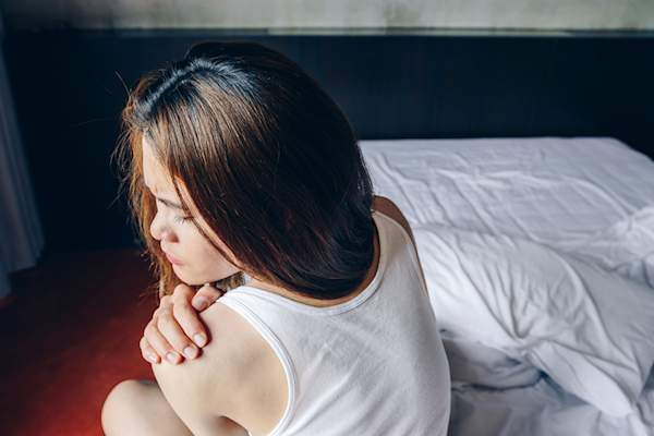 年轻女子在床上痛苦地抱着肩膀