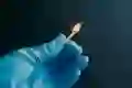 A hand wearing a medical glove holds a lit match