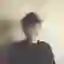 A person standing against a wall, their face is blurred