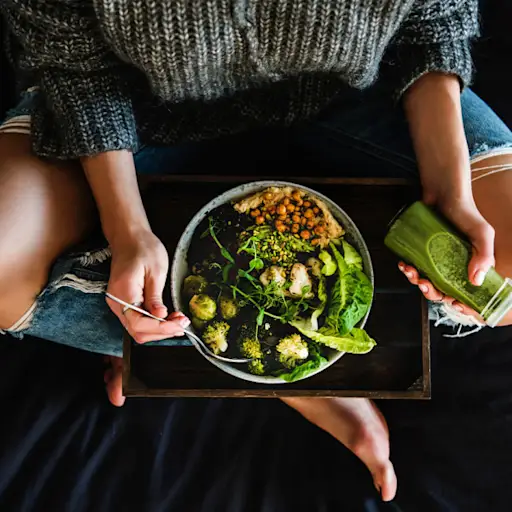 妇女在床上吃素食主义者盘和饮用圆滑的人