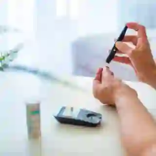 Woman Sitting On Sofa Checking Blood Sugar Level With Glucometer