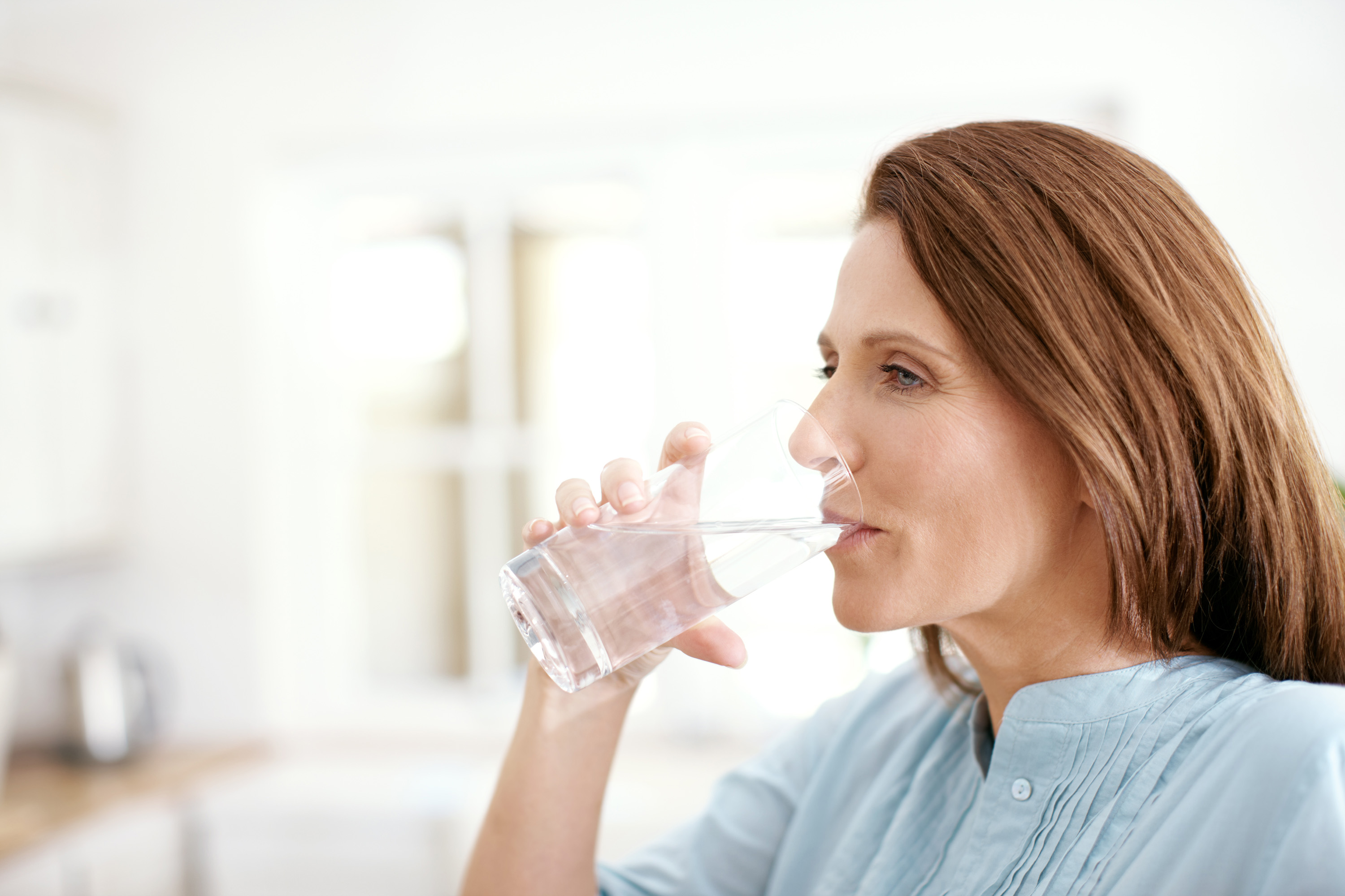 Middle-aged woman drinking a glass of water in a kitchen