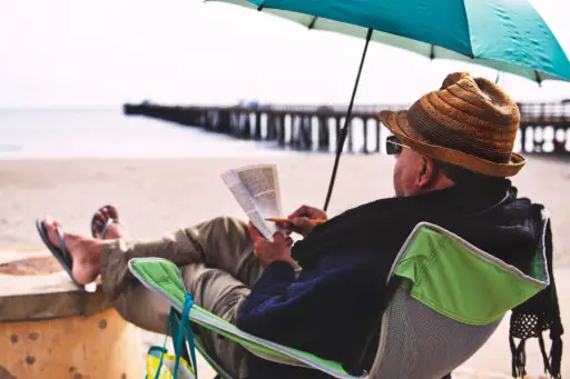 在佩带防晒衣裳的海滩的老人读书