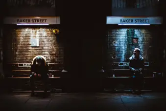 两个男人坐在公共汽车站，一个仰望一个俯视，不同的照明