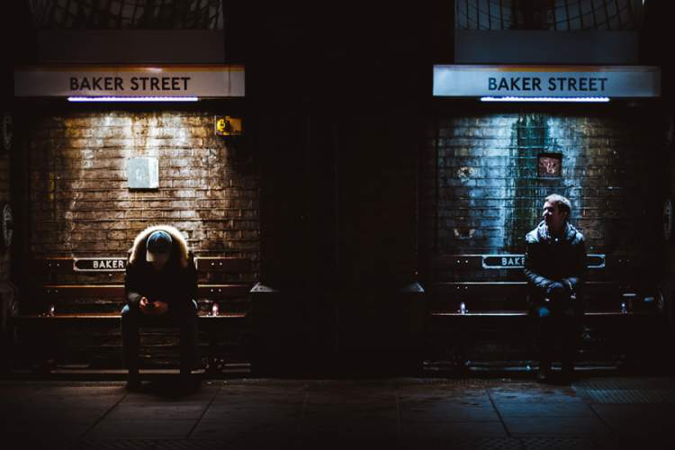 两个男人坐在公交车站，一个向上看，一个向下看，灯光不同