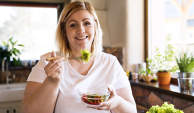快乐的胖女人在厨房里吃沙拉。
