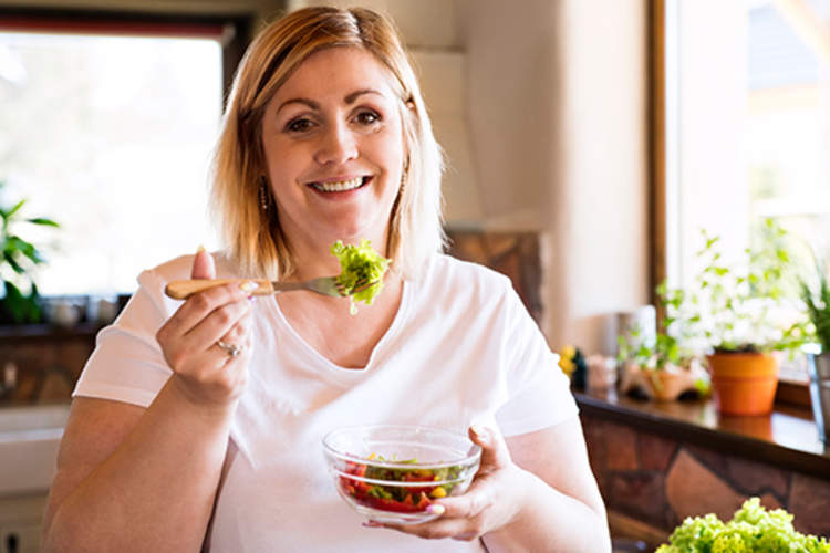 快乐超重的女人吃在厨房沙拉。