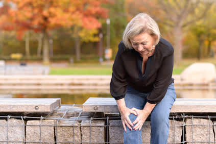 女人抓住她的膝盖，膝盖关节疼痛，而坐在公园。