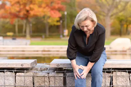 女人抓着膝盖，在公园里坐着膝关节疼痛。