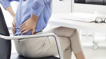 有坐在椅子的低腰疼的妇女在工作。
