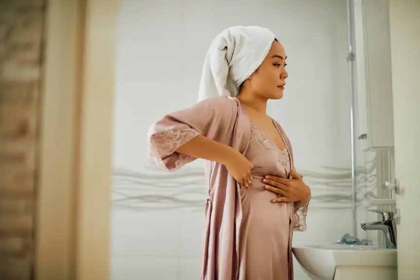 年轻的亚洲女人站在浴室的镜子前,做乳房自我检查