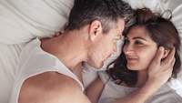 Couple looking at each other lovingly in bed.