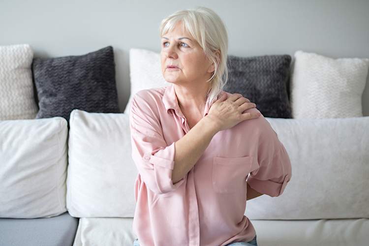 高级的女人在痛苦在家里坐在沙发上。