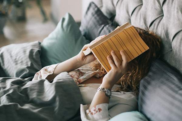 疲惫的女人在床上用书盖着脸