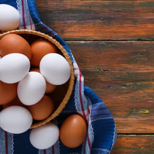 木桌子上的篮子里有白鸡蛋和棕色鸡蛋。