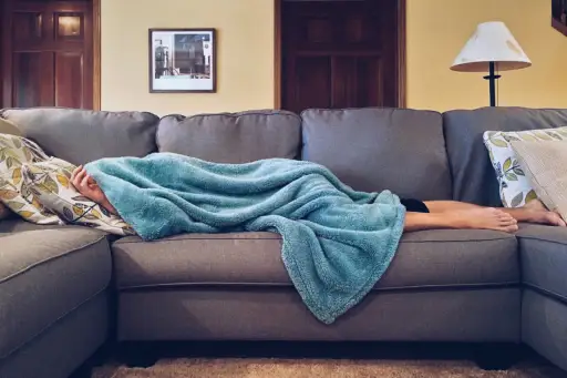 女人在沙发上的毯子下生病