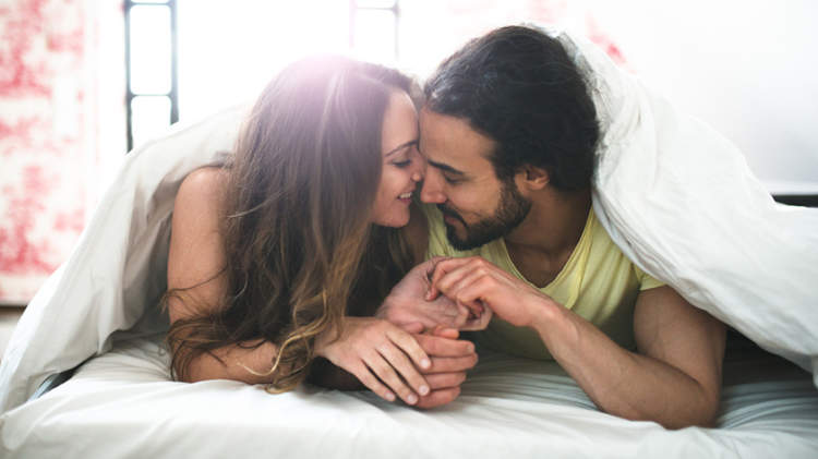 一对年轻的夫妇在床上的被子下互相依偎亲吻。