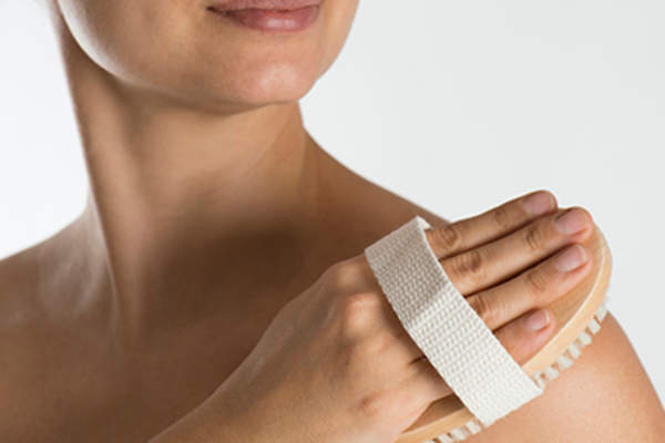 年轻女子轻轻刷她的肩膀的皮肤。