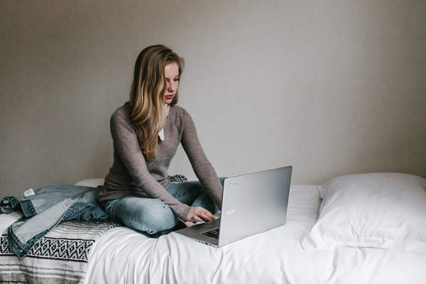 Woman sitting on bed typing on laptop