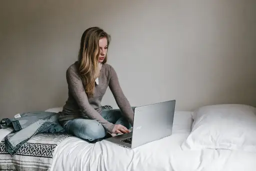 女人坐在床上打字在笔记本电脑上