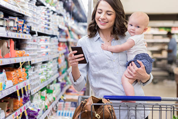 女人在杂货店,抱着她的婴儿,并检查她的期跟踪应用程序。