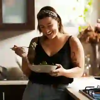 A woman eats a salad in a kitchen