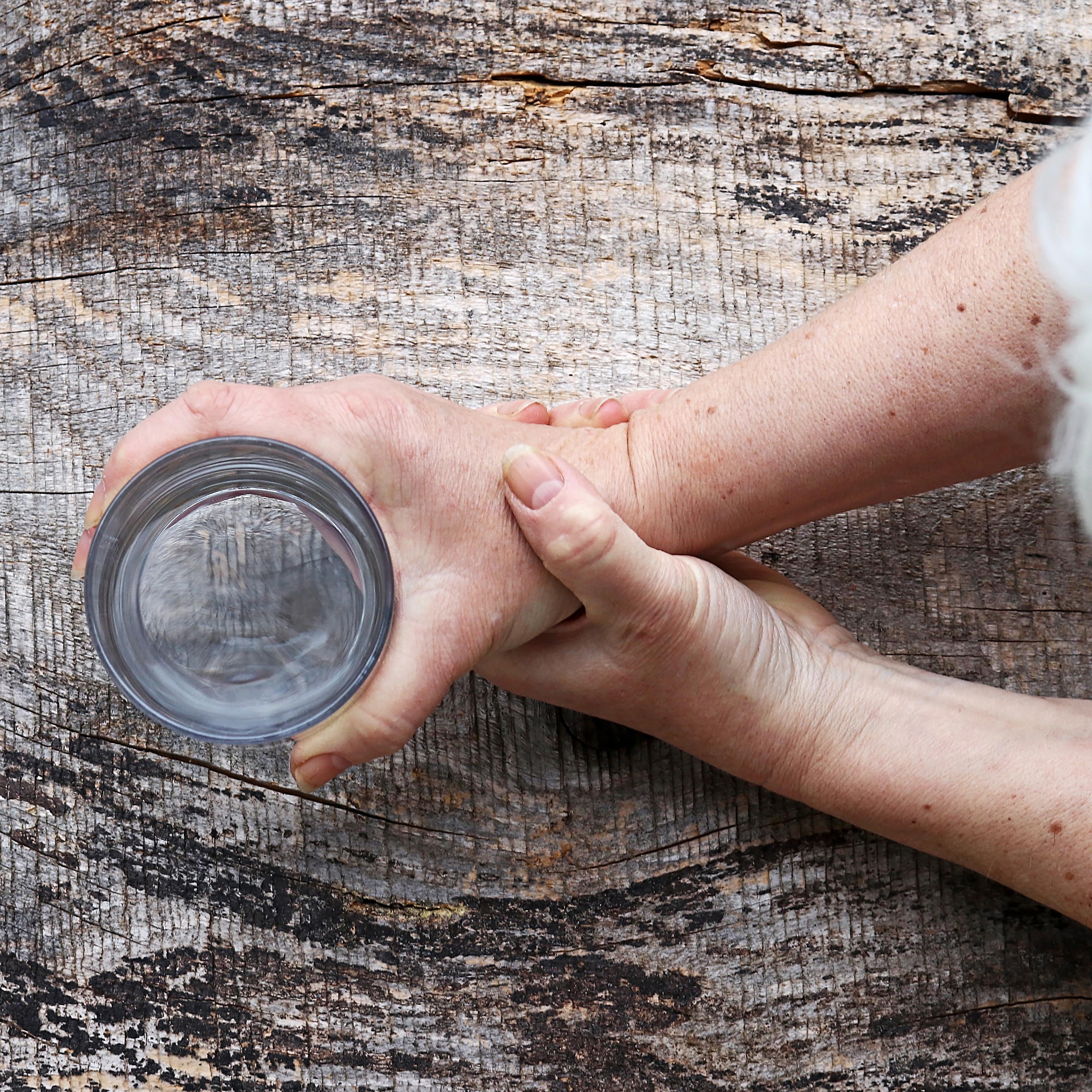 高级用颤抖的手拿着一杯水