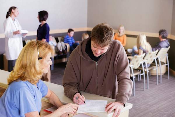 接待员有助于在卫生所的小伙子填写的文书工作。