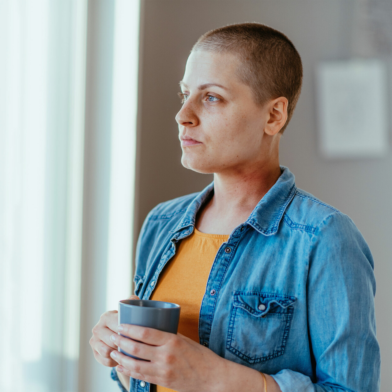 一个剃光头的女人拿着一个杯子向窗外望去