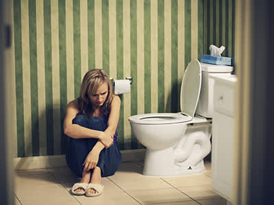 悲伤的年轻女人坐在浴室的地板上。