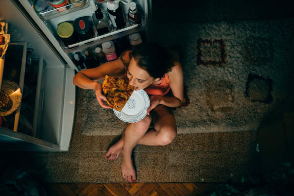 女人在晚上吃比萨饼的冰箱的前坐在地板上