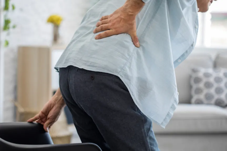Man getting up from chair grabbing lower back in pain.