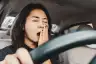 Woman yawning behind the wheel of a car