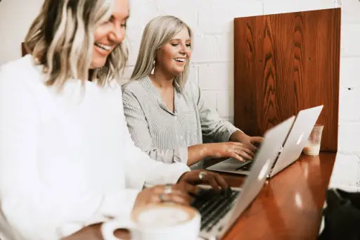 两个女人微笑着在笔记本电脑上打字