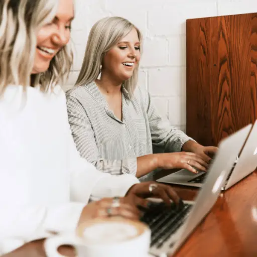 两位女士微笑着在笔记本电脑上打字