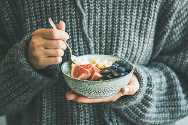 穿灰色羊毛衫的女人在吃水果椰子粥。