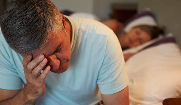 年纪大一些的男人在床上醒着，感到很沮丧。