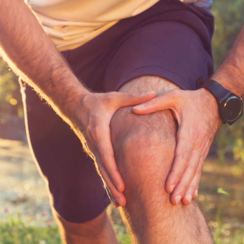 一个膝盖疼痛的跑步者停下来抱住他的膝盖。