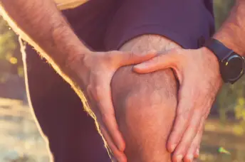 膝盖疼痛的跑步者会停下来握住他的膝盖。