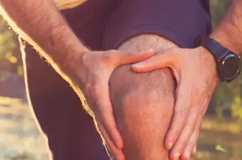 A runner with knee pain stops to hold his knee.