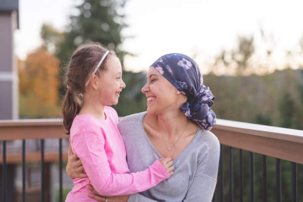 年轻的母亲与癌症微笑的看着女儿