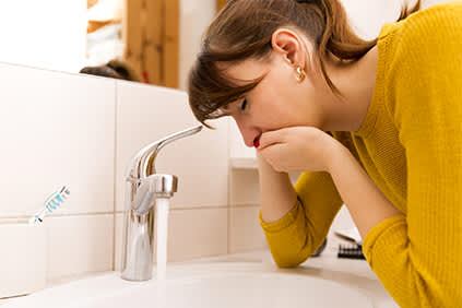 一名患有溃疡性结肠炎的恶心女性斜靠在水槽上，捂着嘴。