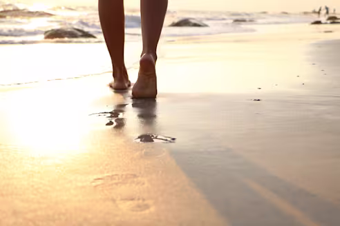 Cropped image of a person walking on a wet sandy beach leaving footprints in the sand during sunset.